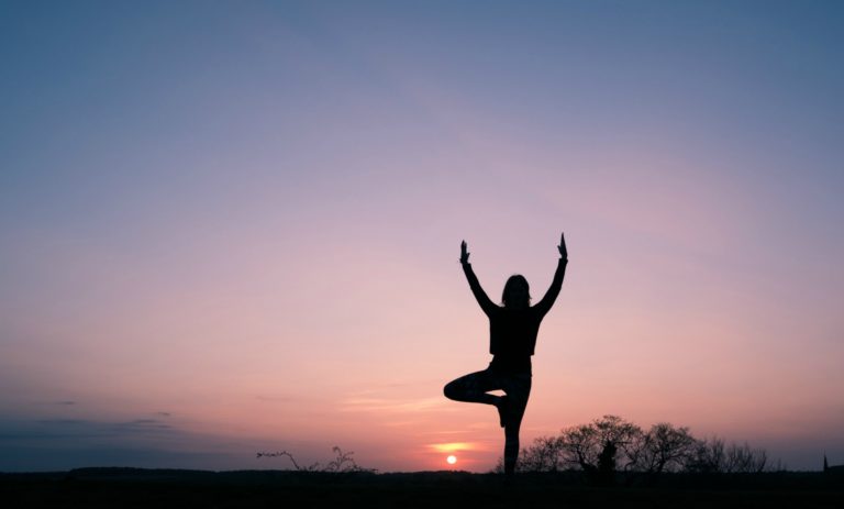 woman doing tree pose at sunset, yoga for cancer blog triyoga