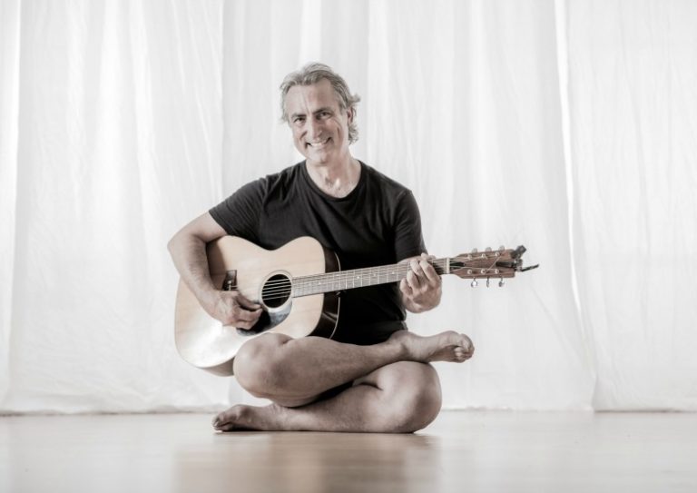 Richard Rosen yoga teacher playing guitar and smiling in studio triyoga