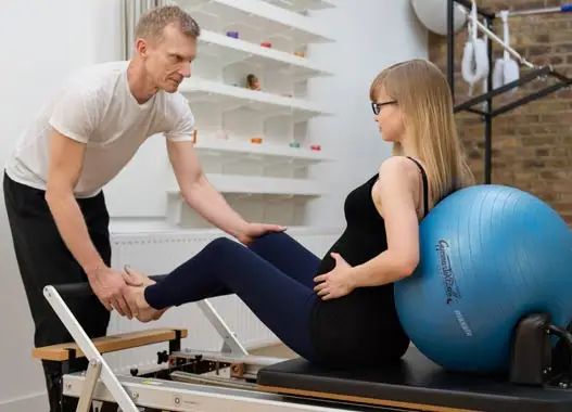A post and prenatal Pilates instructor is guiding a client through a series of exercises.