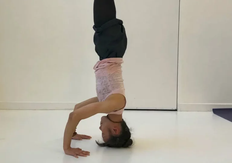 oga instructor Emi Tull is doing a headstand in a Dharma yoga class at Triyoga studio in London. She is balancing on her hands with her feet up in the air. Her body is straight and her face is calm. She is focused on her breath and her practice.