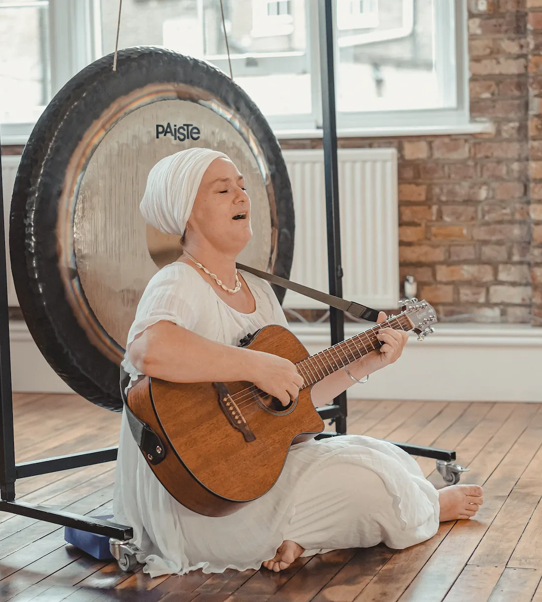 Woman playing guitar beside gong.
